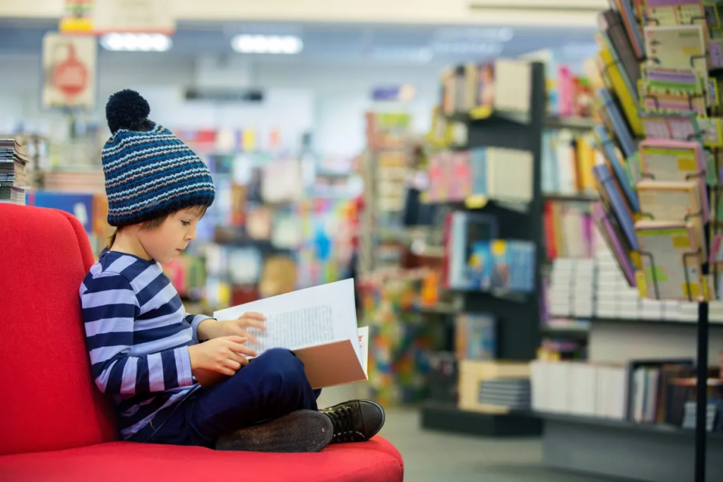 Young Boy Wearing a Beanie Reading a Picture Book in a Library