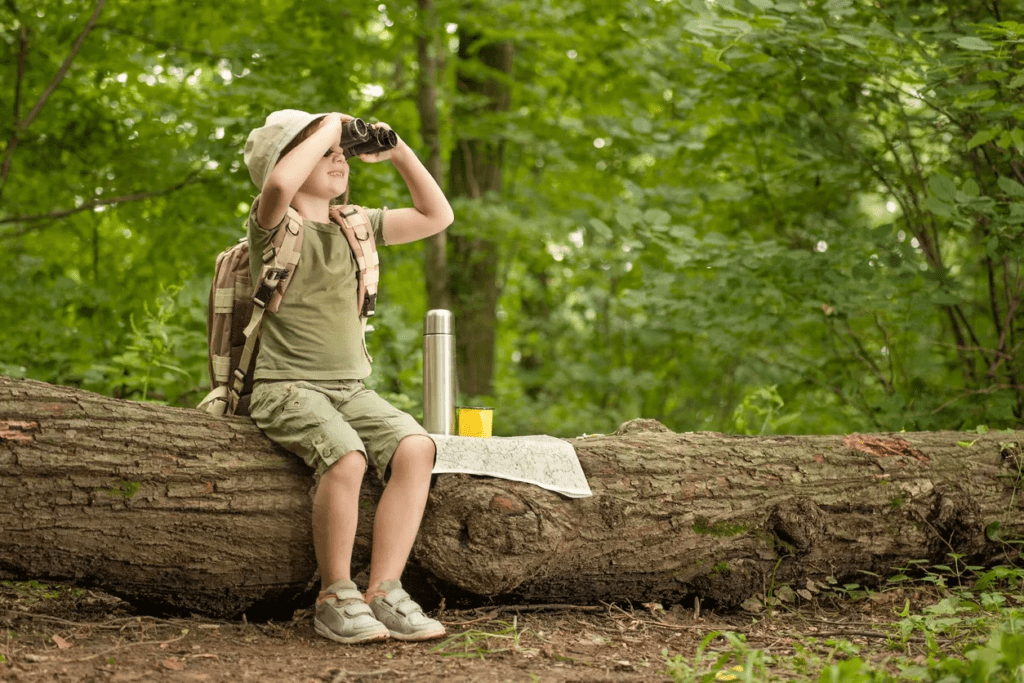 Boy Sitting on a Log in Nature Looking Through Binoculars