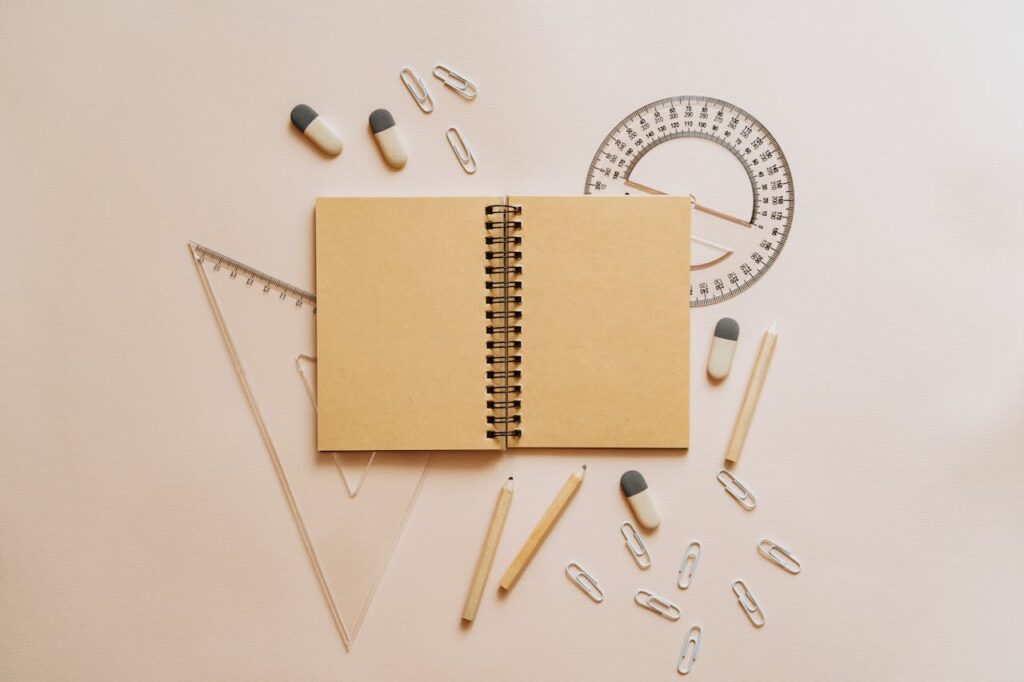 Open Notebook Surrounded by Protractor, Erasers, Pencil, and Paperclips