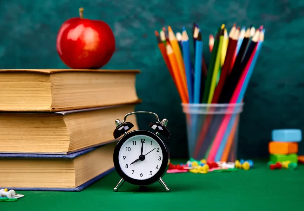 school supplies with colored pencils, an apple, a clock, a stack of books, and thumb tacks