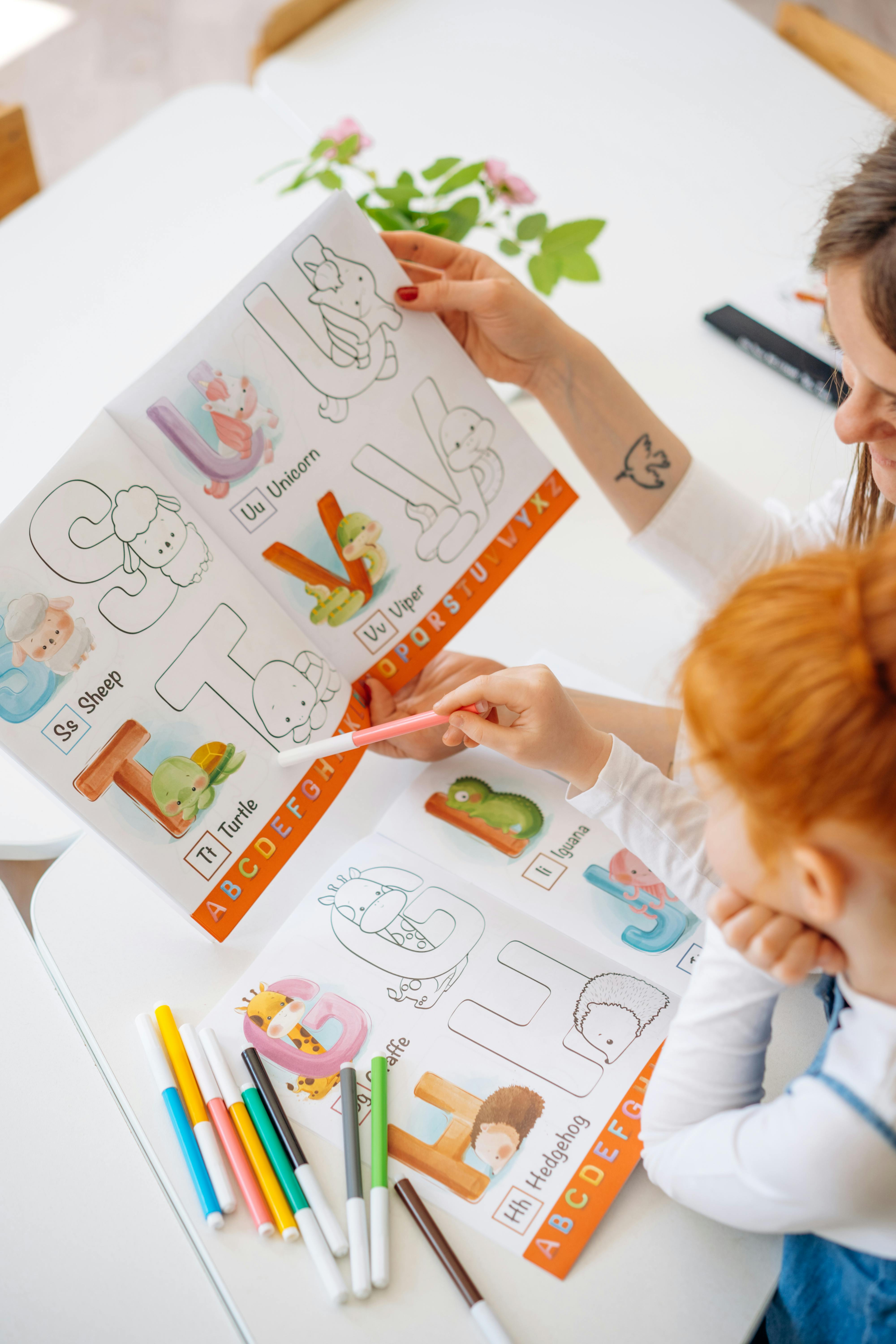 redhead girl looking at a colorful phonics page with markers next to her and her mom helping her